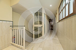 Landing of a residential apartment building with a staircase with cream marble floors, white metal railings and a metal and glass