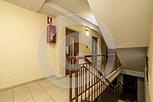 Landing of a residential apartment house with a staircase with light terrazzo floors, red painted metal railings and double