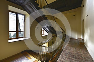 Landing of a vintage house with wooden staircase and metal railing and rustic stoneware floors