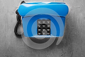 Landline blue phone on a gray wall background