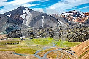 Landmannalaugar, Iceland. Bird View at camping site and mountain hut with many tents and cars, and huge lava field and floods,