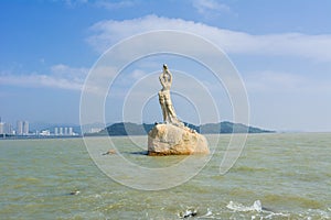 Landmark of Zhuhai city of China. Statue of Fish Woman, fisher girl stature with background of sea, island, and tall buildings