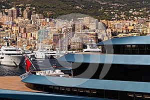 Landmarks of Monaco through decks of huge yacht of blue color in port Hercules at sunny day, glossy board of the motor