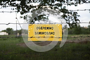 Landmines sign on barbed wires. Translation from Ukrainian language - Danger mines.