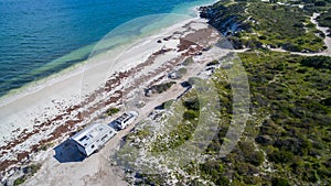 Landscape aerial view of 4WD and modern caravan parked adjacent to a sparkling sunny beach