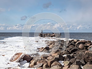 Landscape of Baltic sea and beach with big rocks with ice and snow formations on the shore in bright sunlight. Frozen ice blocks