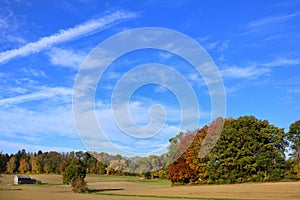 Landscape in Bavaria in autumn, with colorful trees, fields and a wooden house, in front of a blue sky with clouds