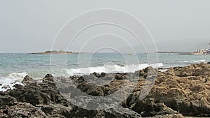 Landscape on beach of Stalis at bay of Malia on Crete Greece. People enjoying the beach. Rocks in water. bars and restaurants in