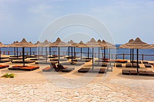 Landscape of beach with wooden sun beds, thatched umbrellas and