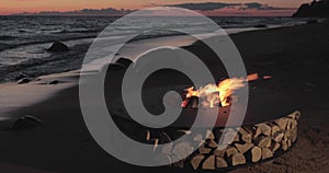 The landscape of the beautiful metal round a fireplace on the sandy coast with a tidal wave at sunset, stones