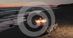 The landscape of the beautiful metal round a fireplace on the sandy coast with a tidal wave at sunset, stones