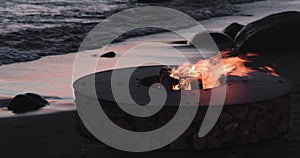 The landscape of the beautiful metal round a fireplace on the sandy coast with a tidal wave at sunset, stones