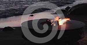 The landscape of the beautiful metal round a fireplace on the sandy coast with a tidal wave at sunset, stones