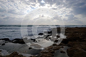 Landscape with beautiful sunset on seacoast with stones in the sea and clouds on the sky