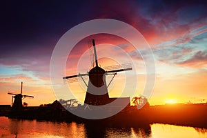 Landscape with beautiful traditional Dutch mill near water courses with fantastic sunset and reflection in water. Netherlands.