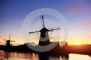 Landscape with beautiful traditional Dutch mill near water courses with fantastic sunset and reflection in water. Netherlands.