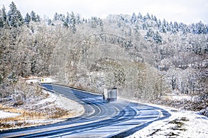 Landscape with big rig semi truck driving on winding winter snow road with snowy forest