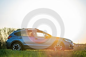 Landscape with blue off road car on green grass at sunset. Traveling by auto, adventure in wildlife, expedition or extreme travel