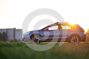 Landscape with blue off road car on green grass at sunset. Traveling by auto, adventure in wildlife, expedition or extreme travel