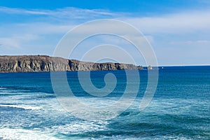 Landscape of the blue sea with a rock along the horizon.