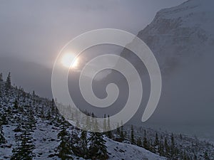 Landscape with bright sun shining through fog at the eastern rock face of Mount Edith Cavell in Jasper National Park, Canada.