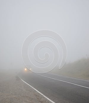 Landscape with a car on the road in the fog with headlights incl