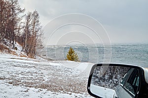 Landscape with car side mirror, trees, snow field and lake on a winter day