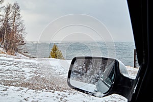 Landscape with car side mirror, trees, snow field and lake on a winter day