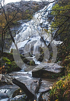 Landscape of cascade Steall Waterfall on wet rocks in autumn in the forest, Scotland