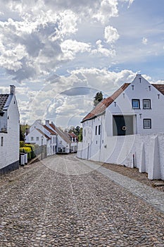 Landscape of cobbled street between houses with white walls against blue sky covered with clouds