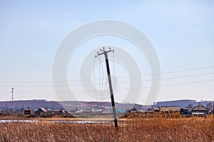 Landscape in a deserted place in nature with high yellow grass in the field and an old tall wooden post with dangling electrical