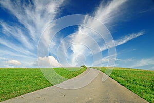 Landscape, dirty road among green fields, blue sky in the backgr