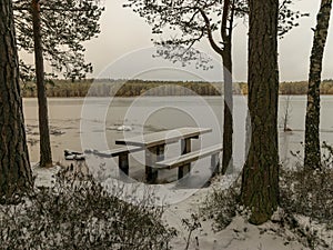 Landscape with flooded lake shore, picnic area covered with ice