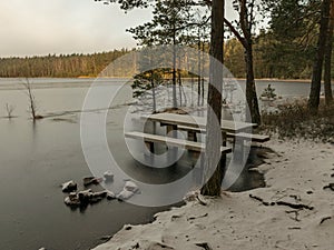 Landscape with flooded lake shore, picnic area covered with ice