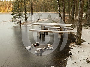 Landscape with flooded lake shore, picnic area covered with ice