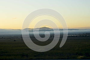 a landscape of fog over a field and a sunset over a river