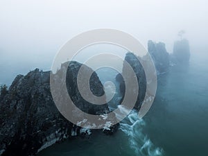 A landscape with fog, pointed cliffs in blue water in cloudy weather in the morning