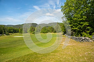 Landscape on a golf course with green grass, trees, beautiful blue sky and stone fence