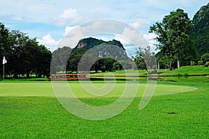 Landscape of a golf field with green grass,water hazard, trees, and mountain under cloudy blue sky 1