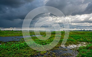 Landscape of green grass field and overcast sky. Dark cloudscape of a stormy sky. Natural water reservoir. Water sustainability.