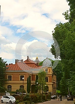 A landscape, a house, a building made of bricks. At the base of yellow color, the main part is brown, the roof is red. There is a