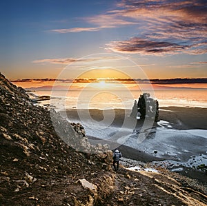 Landscape Hvitserkur in Iceland, young traveling hiking down from cliff to black sand beach in sunset