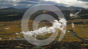 Landscape of icelandic valley with mountains and geothermal plant with steam in sunny fall day