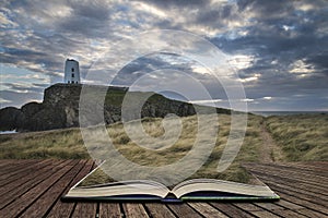 Landscape image of Twr Mawr lighthouse with windy grassy footpath in foreground at sunset concept coming out of pages in book