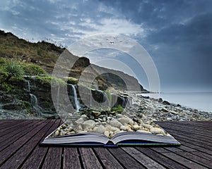 Landscape image of wide waterfall flowing onto rocky beach at sunrise conceptual book image