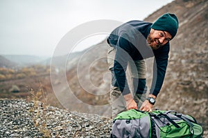 Landscape image of young hiker man hiking in mountains with travel backpack. Traveler bearded male preparing his backpack