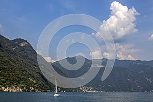 Landscape of Lake Como - white yacht in blue waters, alpine hills and scenic sky.