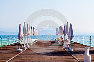 Landscape Lake Garda with pier, beach chairs and umbrellas in the foreground, Italy