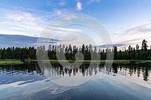 Landscape of lakeshore with pine trees and an expressive sky reflected in the water