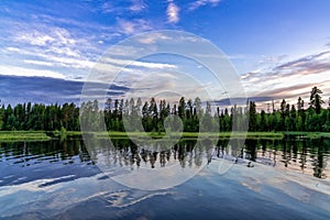 Landscape of lakeshore with pine trees and an expressive sky reflected in the water